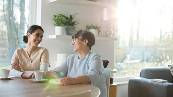 10-TIPS-FOR-COMMUNICATING-WITH-SOMEONE-WITH-DEMENTIA-1 A caregiver sitting with a senior woman at a table