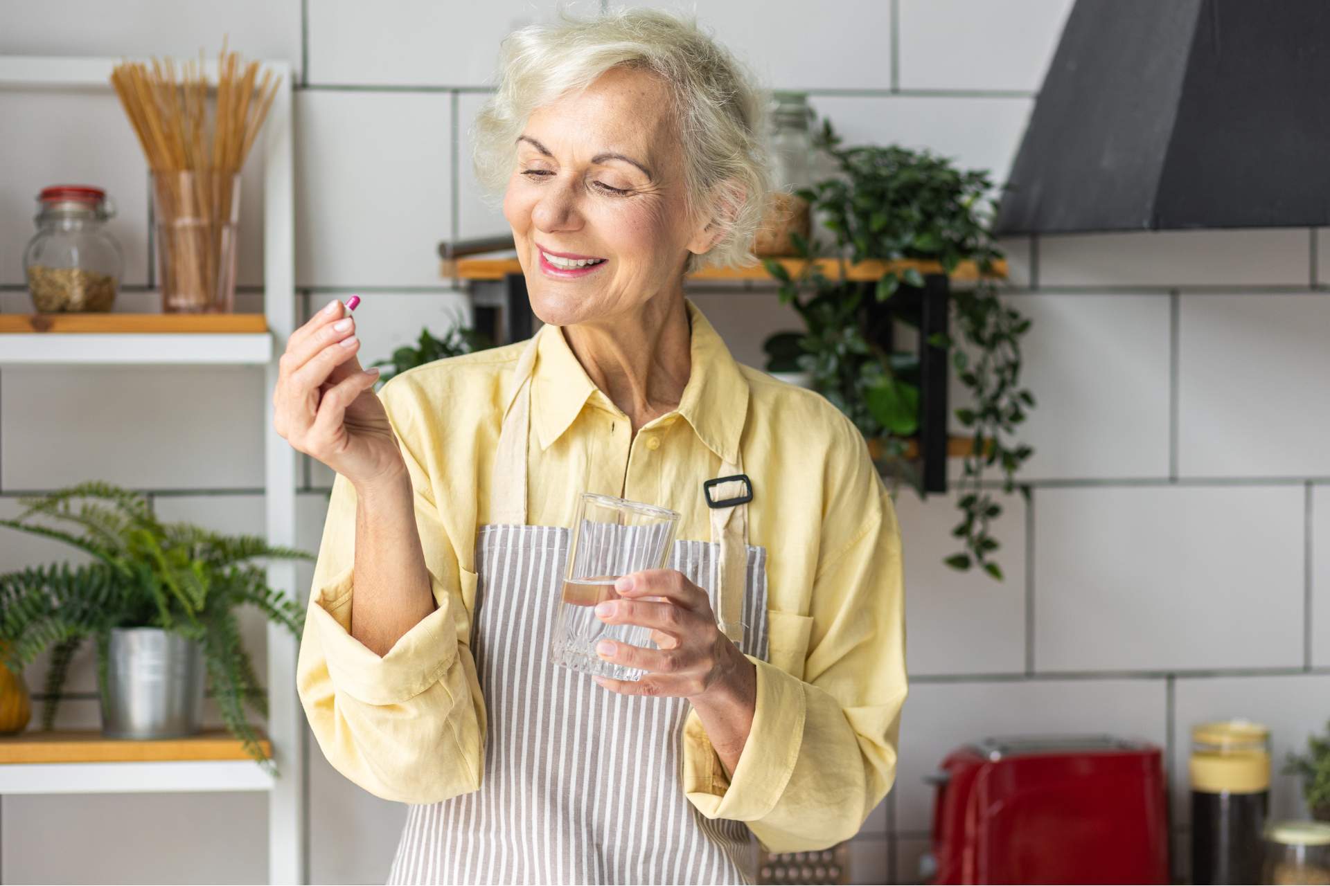 Senior woman smiling with a glass of water and two supplements